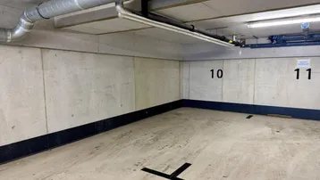 Geräumiger Tiefgaragenstellplatz mit robusten Betonwänden und freiliegenden Versorgungsleitungen an der Decke, ideal für sicheres Parken.