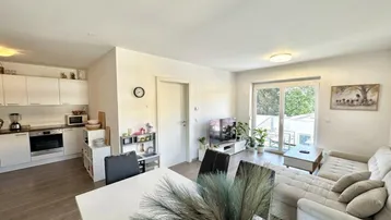 Heller offener Wohn-Essbereich mit integrierter Küche, modernem Sofa und Zugang zum Balkon.
