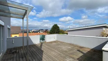 Große Dachterrasse mit Holzboden und Überdachung, bietet weite Ausblicke unter blauem Himmel.