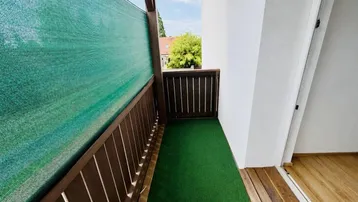 Balkon mit grünem Sichtschutz, Kunstrasen und Holzboden für entspannte Stunden im Freien.