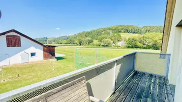 Geräumiger Balkon mit Holzboden und weitem Blick ins Grüne und auf die Landschaft.