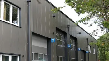 Moderne Gewerbeimmobilie mit mehreren Garagentoren und großen Fenstern, umgeben von Bäumen und Parkplätzen.