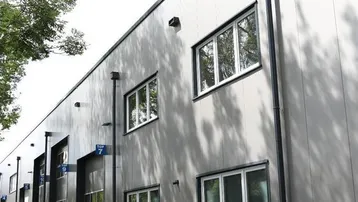 Moderne Gewerbeimmobilie mit grauer Fassade, großen Fenstern und Parkplätzen im Freien.