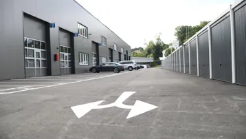 Ansicht einer modernen Gewerbeimmobilie mit mehreren Garagen- oder Lagereinheiten und einem asphaltierten Zufahrtsweg.