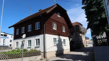 Traditionelles Wohnhaus mit brauner Holzfassade und weißem Putz in ländlicher Umgebung.
