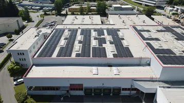 Luftaufnahme des Hauptgebäudes eines Industriekomplexes mit einer großen Photovoltaikanlage auf dem Dach.