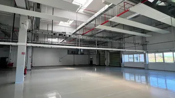 Große, leere Industriehalle mit hohen Decken, glänzendem Boden und sichtbaren Lüftungssystemen.