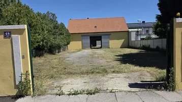 Gelbes Gebäude mit rotem Ziegeldach und großem Tor, umgeben von Bäumen und einem Schotterweg.