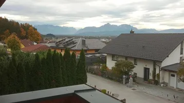 Blick über eine Wohnsiedlung mit Häusern und Photovoltaikanlagen auf Dächern, im Hintergrund Berge.