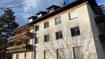 Mehrstöckiges Wohngebäude mit traditionellen Holzbalkonen und Satteldach unter bewölktem Himmel.
