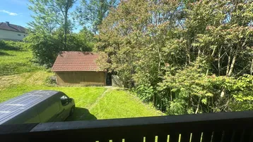 Blick von einem Balkon auf einen Schuppen, Bäume und einen Lieferwagen im Grünen.