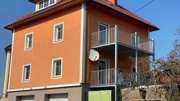 Wohnhaus mit oranger Fassade, Satteldach und zwei Balkonen, sowie Garagen im Erdgeschoss.