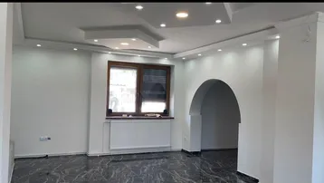 Heller Wohnraum mit modernem Deckenlicht, dunklem Marmorboden und elegantem Rundbogen.