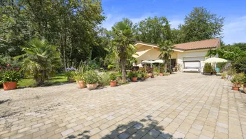 Geräumige gepflasterte Auffahrt führt zum Haus mit üppigem Garten und Palmen.