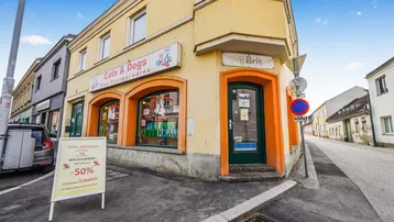 Gelbes Eckgebäude mit Ladenfront und großen Schaufenstern an einer städtischen Straße.