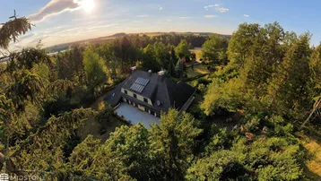 Luftaufnahme eines Hauses umgeben von üppigem Grün mit Solarpaneelen auf dem Dach bei Sonnenuntergang.