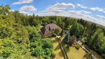 Weitläufige Luftaufnahme des Anwesens, eingebettet in eine grüne Waldlandschaft unter blauem Himmel.