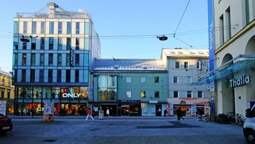 Blick auf eine belebte Einkaufsstraße mit modernen und traditionellen Gebäuden unter blauem Himmel.