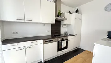 Moderne Einbauküche mit weißen Schränken, dunkler Arbeitsplatte und Induktionskochfeld.