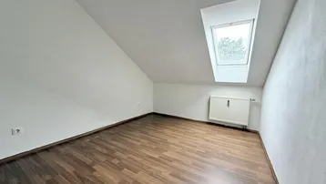 Heller Raum im Dachgeschoss mit Schrägdecke, Dachfenster und Laminatboden.