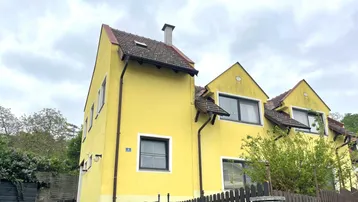 Gelbes Haus mit Satteldach und mehreren Fenstern unter bewölktem Himmel.