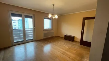 Helles Wohnzimmer mit Parkettboden, gelben Wänden und Zugang zu einem Balkon.