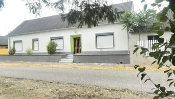 Weißes Einfamilienhaus mit grünem Eingangsbereich und grauen Fensterläden an einer ruhigen Straße.