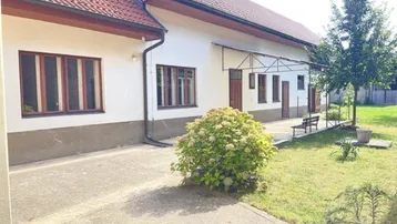 Ländliches Haus mit weißer Fassade, rotem Ziegeldach und einem gepflegten Vorgartenbereich.