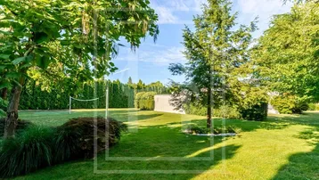 Weitläufiger grüner Garten mit Rasenfläche, hohen Hecken und einem Volleyballnetz für Freizeitaktivitäten.