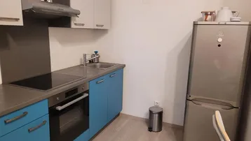 Funktionale Küche mit blauen Unterschränken, Induktionskochfeld und einem freistehenden Kühlschrank.
