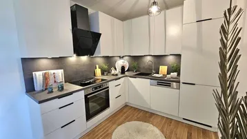 Moderne Einbauküche mit weißen Schränken, dunkler Arbeitsplatte und Holzboden.