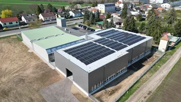 Luftaufnahme eines modernen Industriegebäudes mit Photovoltaikanlage auf dem Dach und umliegender Landschaft.
