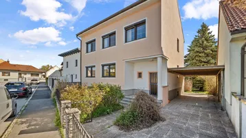 Ansicht des Einfamilienhauses mit beigefarbener Fassade, Rollläden und überdachtem Carport.
