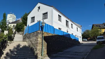 Weißes Wohnhaus mit blauem Zaun und Treppenaufgang in sonniger Umgebung.