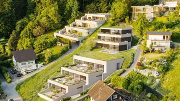Moderne Terrassenhäuser mit Gründächern und Pools, harmonisch in die grüne Hanglandschaft integriert.