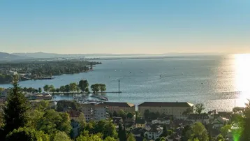 Panoramablick auf eine Stadt am See mit Bergen im Hintergrund bei Sonnenuntergang.