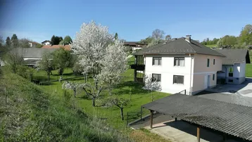 Weitläufiger Blick auf das Wohnhaus mit großem Garten und blühenden Bäumen in ländlicher Umgebung.