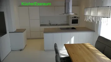 Moderne Küche mit weißer Einbauküche, Kochinsel und Esstisch unter Holzbalkendecke.