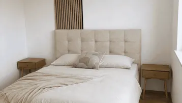 Helles Schlafzimmer mit beigem Polsterbett, Holznachttischen und dekorativer Wandverkleidung.