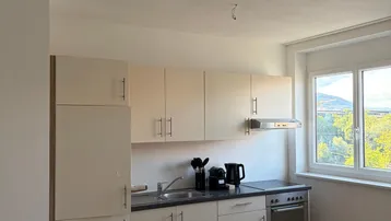 Funktionale Küchenzeile mit hellen Schränken, integriertem Ofen und Fenster mit Ausblick.