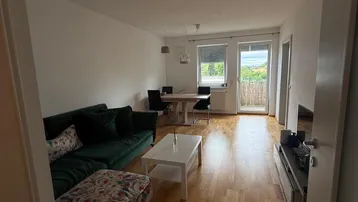 Heller Wohn- und Essbereich mit Holzboden, gemütlichem Sofa und Zugang zu einem Balkon.