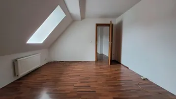 Heller Raum im Dachgeschoss mit Holzboden, Dachfenster und Heizkörper an der Wand.
