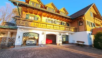 Traditionelles Holzhaus mit Garagen und gepflasterter Auffahrt unter blauem Himmel.