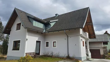 Hausfassade mit Satteldach, kleinen Fenstern und einem kleinen Vorgarten in ländlicher Umgebung.