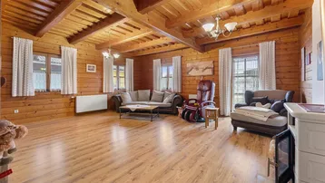 Gemütliches Wohnzimmer im Landhausstil mit Holzwänden, Holzbalkendecke und Laminatboden.