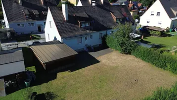 Luftaufnahme eines Einfamilienhauses mit großem Garten, Carport und angrenzender Hecke.