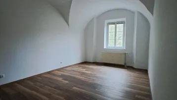 Heller Raum mit einzigartiger Gewölbedecke, Laminatboden und einem Fenster mit Blick ins Grüne.