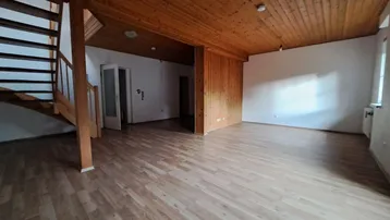 Geräumiges Wohnzimmer mit Holzdecken, Laminatboden und offener Holztreppe zum Obergeschoss.