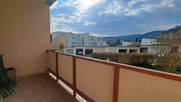 Sonniger Balkon mit Fliesenboden und Blick auf die umliegende Wohngegend und Berge.