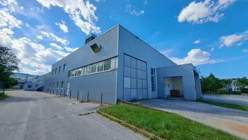 Großes Industriegebäude mit grauer Fassade, vielen Fenstern und einer Laderampe unter blauem Himmel.